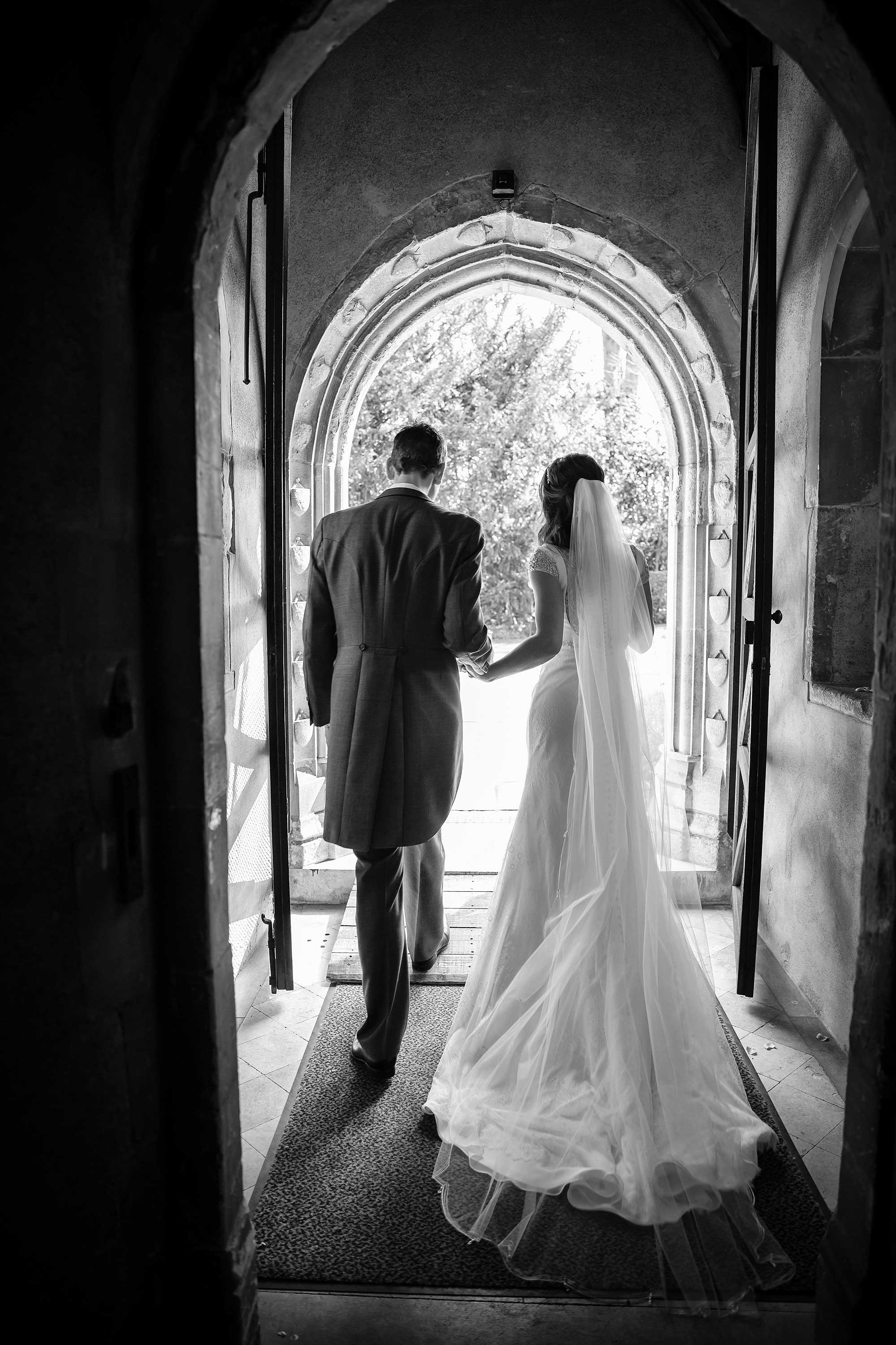 Black and white image of the couple exiting the church taken from behind them, so you can see the back of the brides dress.