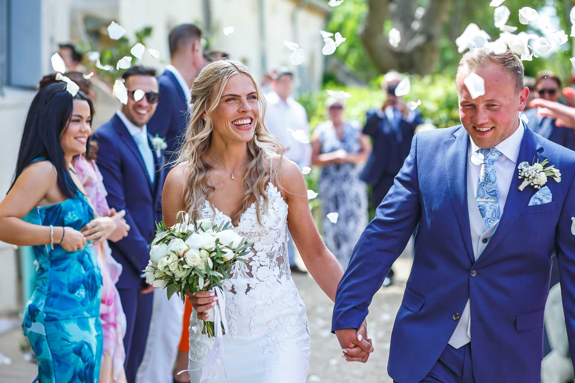 Bride and groom walking through white confetti after their wedding ceremony in France