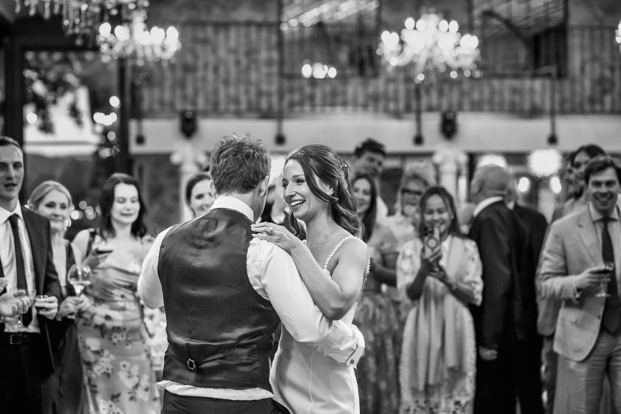 Bride laughing with her groom during their first dance as wedding guests watch